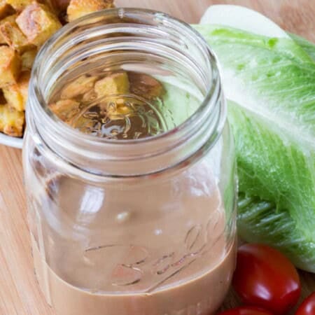 Lettuce, tomatoes, croutons, and a jar of salad dressing on a wooden board.