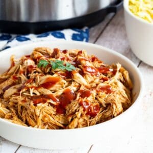 A bowl of barbecue pulled chicken with an Instant pot in the background.