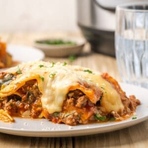 A slice of instant pot gluten free lasagna on a plate with the melting cheese dripping down the sides of the lasagna.
